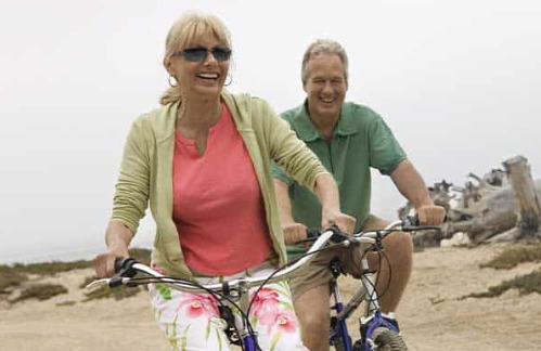 Elderly couple cycling on a beach after knee replacement surgery