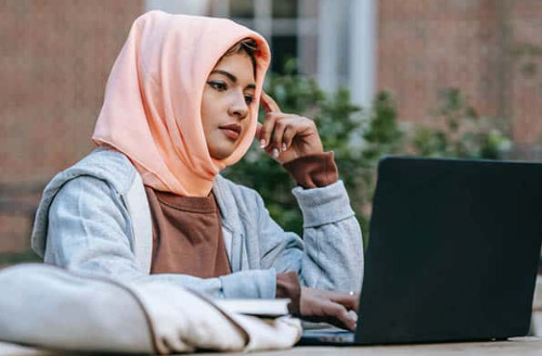 Jobseeker wearing headscarf works on her nursing CV at a laptop