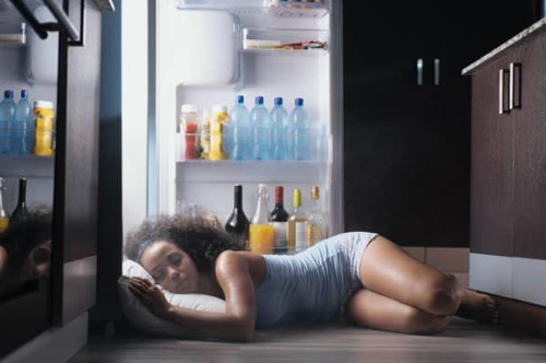 Woman sleeping by an open fridge to stay cool at night