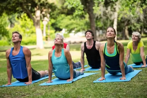 A group of men and women practising yoga and stretches on yoga mats outside