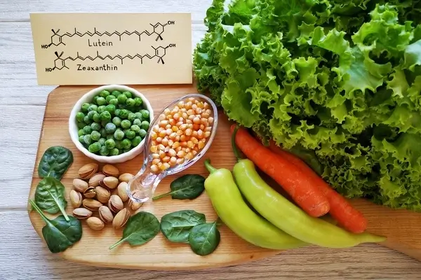 A variety of healthy foods on a wooden chopping board, including pistachios, peas and peppers.