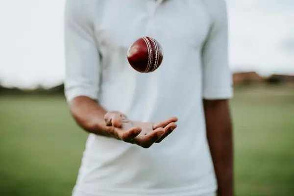 Man dressed in white on a field throwing ball from palm of his hand