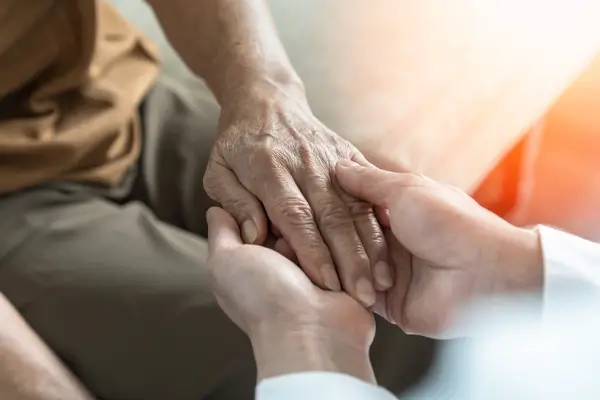 A medical professional holds an elderly parent's hand