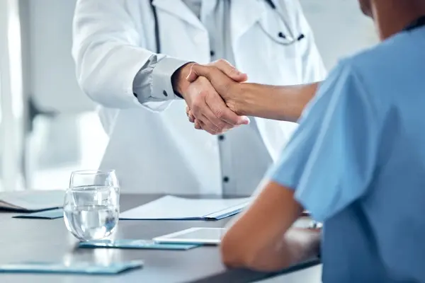 Private healthcare professional in a white coat shakes hands over a table