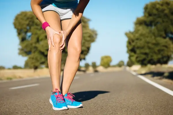Woman experiencing knee pain standing on a road in trainers