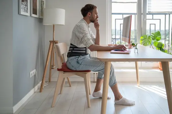 Man researches hernia surgery in London at a desk wearing a brace